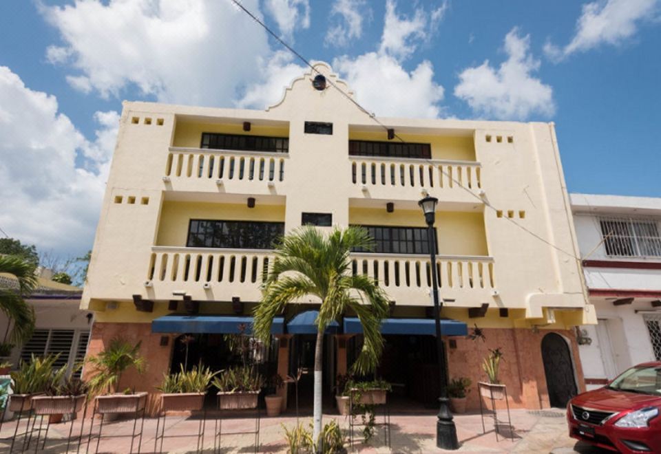 a two - story building with a balcony and blue awnings is surrounded by palm trees and potted plants at Flamingo Hotel