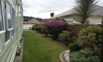 a well - maintained garden with lush green grass , purple flowers , and various plants , set against a cloudy sky at Asure Green Gables Motel