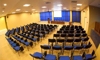 an empty conference room with rows of blue chairs and a large screen at the front at Grand Hotel