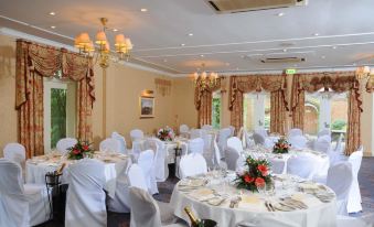 a well - decorated banquet hall with multiple tables set up for a formal event , including white tablecloths and chairs at Coulsdon Manor Hotel and Golf Club