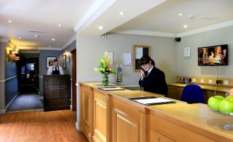 a man wearing a face mask is sitting at a desk in a hotel lobby , talking on his cell phone at Macdonald Craxton Wood Hotel