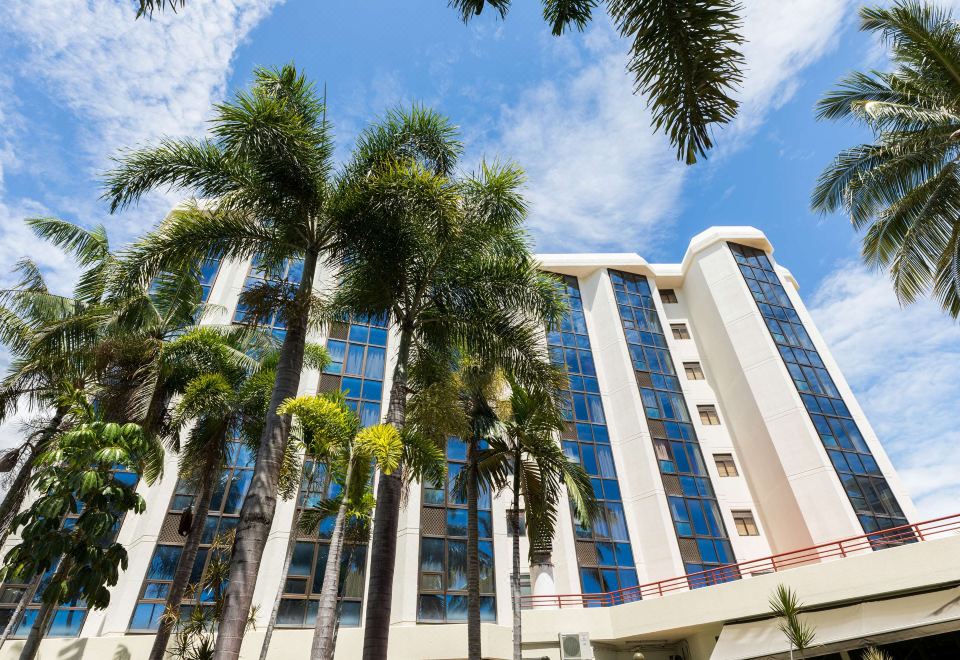 a tall building with blue windows and palm trees in front of it under a blue sky at Rydges Southbank Townsville, an EVT hotel