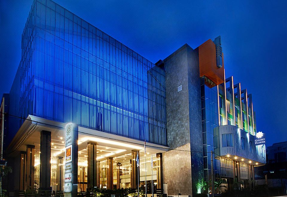 a modern building with a glass facade is lit up at night , and cars on the street below at Golden Flower by Kagum Hotels