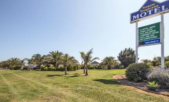 a grassy field with a large building in the background and palm trees in the foreground at Torquay Tropicana Motel