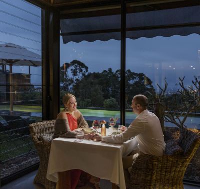 a couple is having dinner at a restaurant with a view of the ocean , and the table is set with wine glasses and candles at Spicers Sangoma Retreat