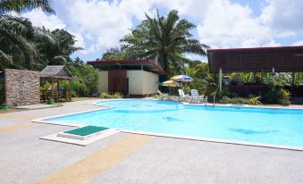 a large swimming pool surrounded by palm trees , with several lounge chairs and umbrellas placed around it at Nampueng Resort