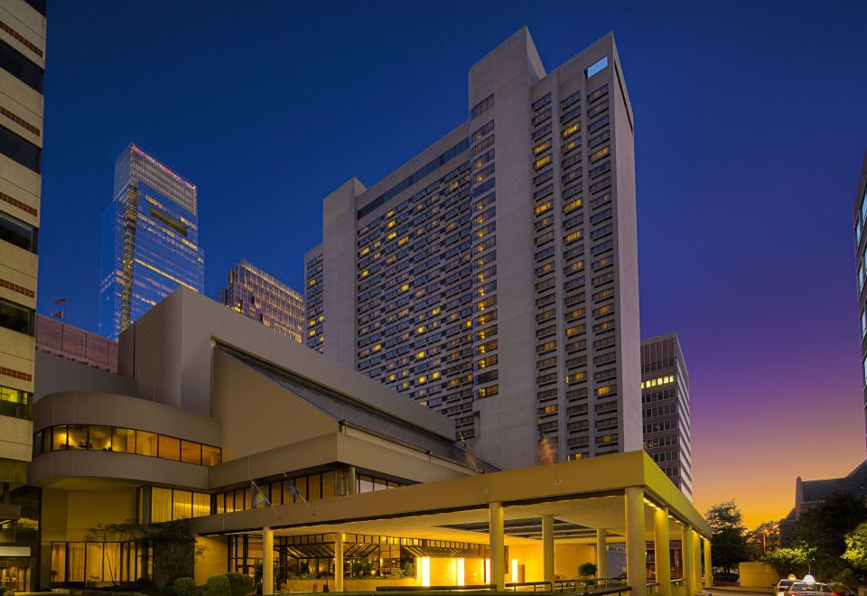 a modern hotel building with large windows , surrounded by modern skyscrapers at night , illuminated by lights at Sheraton Philadelphia Downtown