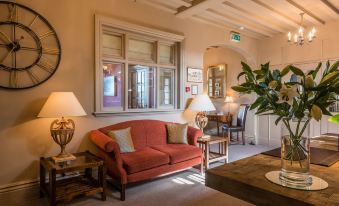 a cozy living room with a red couch , wooden table , and two potted plants on either side of the couch at Colwall Park - Hotel, Bar & Restaurant