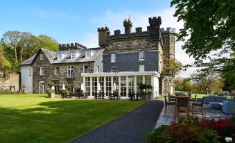 a large stone building with a white porch and green lawn , surrounded by trees and benches at Portmeirion Village & Castell Deudraeth