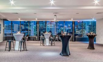 a modern bar with large windows offering a city view , tables set for drinks and people sitting at the bar , and comfortable seating arrangements at Mercure Brisbane Spring Hill