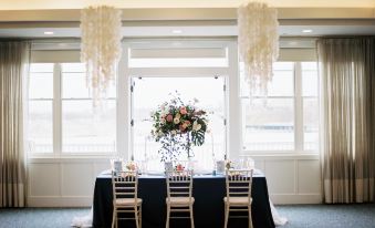 a wedding table with a black tablecloth , white chairs , and a centerpiece in front of large windows at The Inn at Harbor Shores