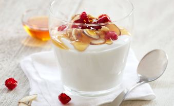 a glass of yogurt with fruit and nuts on a wooden table , accompanied by a spoon at Residence Inn Waldorf