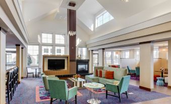 a large , open room with a high ceiling and tall windows has several couches and chairs arranged around a fireplace at Residence Inn Auburn