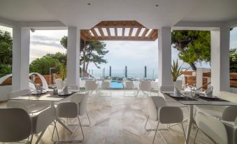 an outdoor dining area with white chairs and tables , overlooking a pool and the ocean at Poseidon Hotel