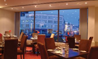 a large dining room with multiple tables and chairs , all facing a large window overlooking a cityscape at The Dragon Hotel