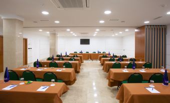 a conference room with multiple tables covered in green tablecloths and chairs arranged in rows at NH San Pedro