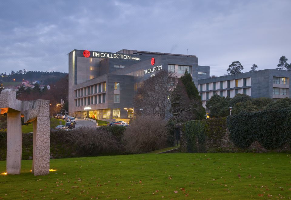 "a large building with the name "" la collection "" lit up in red , surrounded by green grass and trees" at NH Collection Santiago de Compostela