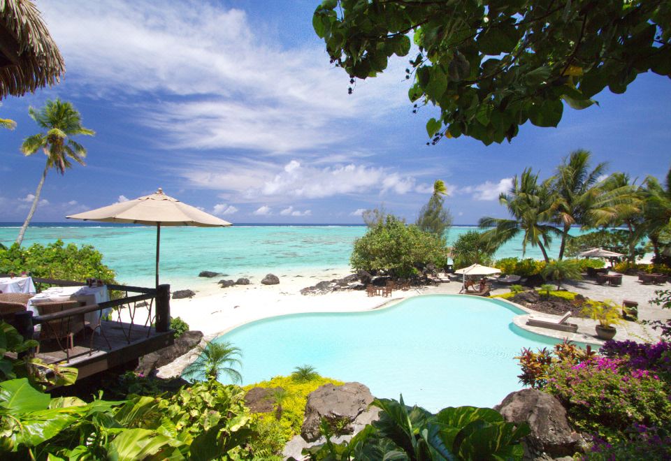 a tropical resort with a large swimming pool , surrounded by lush greenery and a beautiful view of the ocean at Pacific Resort Aitutaki - Adults Only