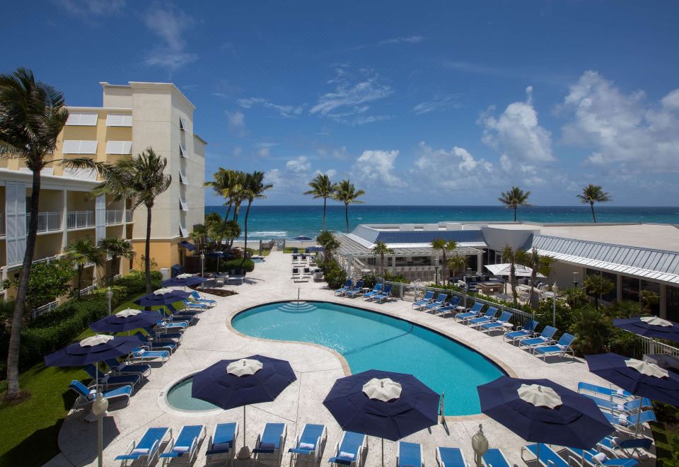 a resort with a large pool surrounded by lounge chairs and umbrellas , providing a relaxing atmosphere for guests at Delray Sands Resort