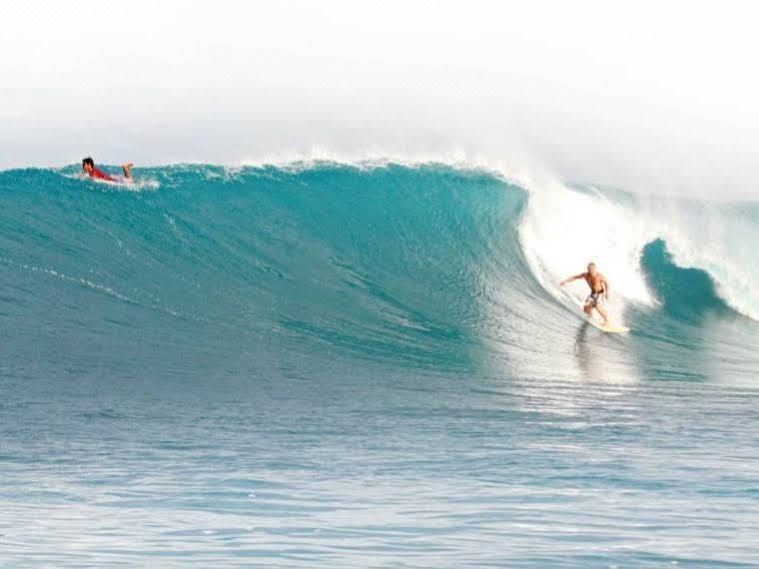 a surfer is riding a large wave in the ocean , with another surfer visible in the background at Hollow Tree's Resort