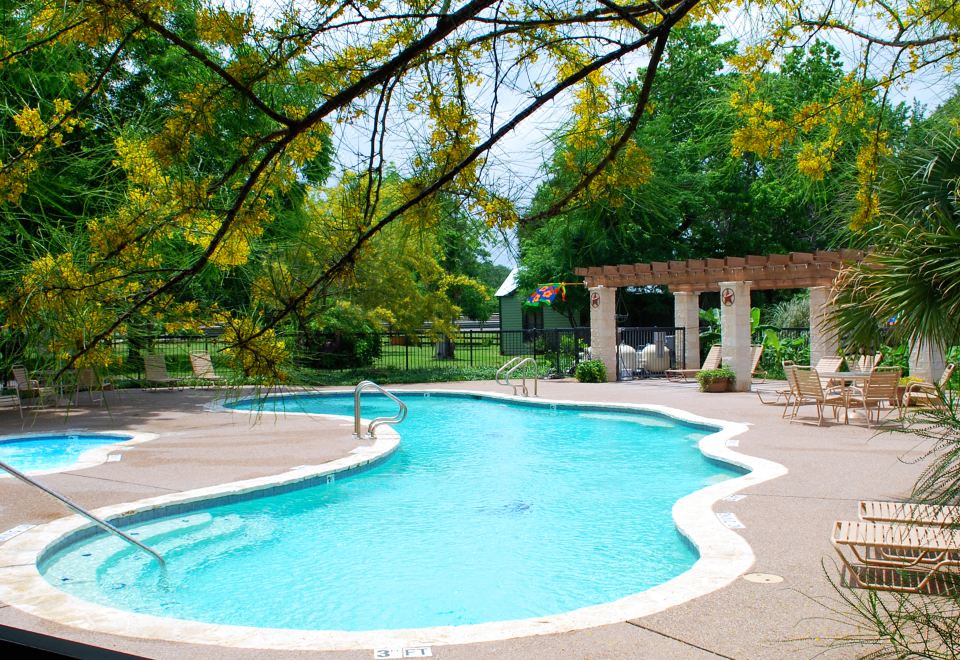 a large outdoor swimming pool surrounded by grass and trees , with several lounge chairs placed around the pool area at North Texas Jellystone Park