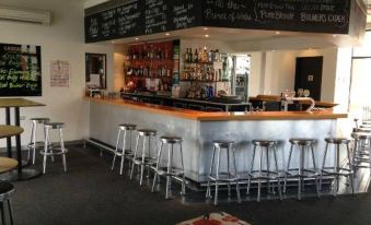 a modern bar with a bar counter , several stools , and a chalkboard menu on the wall at Prince of Wales Hotel