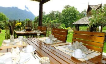 a wooden table with plates , cups , and silverware is set up under a covered patio area at Aurora Resort Chiangdao