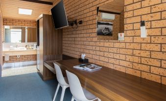 a room with a brick wall , wooden table , and two white chairs in front of a tv at Maffra Motor Inn
