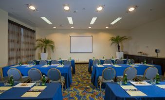 a conference room with blue tables and chairs , a projector screen , and palm trees at Hodelpa Garden Court