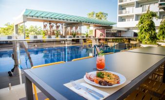 a table with a plate of food , a glass of drink , and a napkin is set up near a pool at Rydges Palmerston - Darwin, an EVT hotel