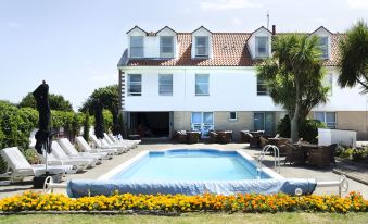 a large swimming pool is surrounded by lounge chairs and a house with yellow flowers in the front yard at Beachcombers Hotel