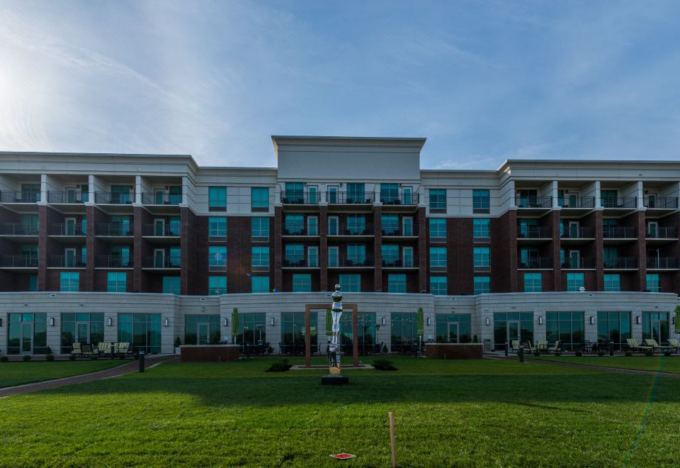 a large white building with multiple floors , surrounded by green grass and trees , under a clear blue sky at Holiday Inn Owensboro Riverfront