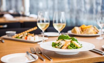 a dining table with a white plate of salad , two wine glasses , and two forks placed on it at Park Inn by Radisson Central Tallinn