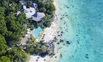 aerial view of a large resort on a tropical island with a swimming pool , surrounded by palm trees and the ocean at Small Luxury Hotels of the World - Pacific Resort Aitutaki
