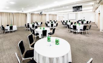 a large conference room with multiple round tables , black chairs , and white tablecloths , surrounded by windows and a screen at Park Inn by Radisson Krakow