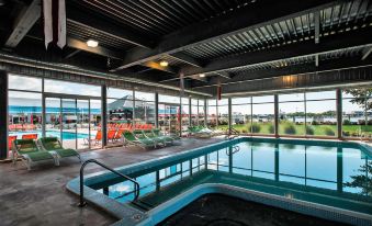 an indoor swimming pool surrounded by lounge chairs , with people relaxing and enjoying the view outside at Holiday Inn Grand Haven-Spring Lake