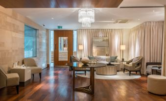 a spacious living room with hardwood floors , a glass coffee table , and a chandelier hanging from the ceiling at Lucknam Park Hotel