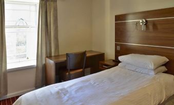 a clean , well - organized hotel room with a bed , desk , and window , along with some personal items at County Hotel