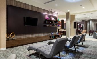 a modern living room with two lounge chairs , a television mounted on the wall , and shelves filled with various items at Courtyard Elmira Horseheads