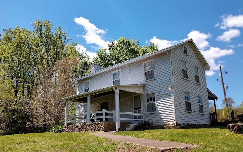 a two - story house with a white roof and porch is surrounded by trees and grass at Graves Mountain Farm & Lodges