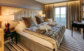 a large bed with a luxurious comforter and pillows is situated in a room with striped carpet and a window at Ingliston Country Club Hotel