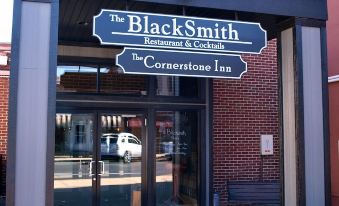 "a black and white photo of a brick building with a sign that reads "" the blacksmith & cocktail ."" the photo depicts the entrance" at Cornerstone Inn