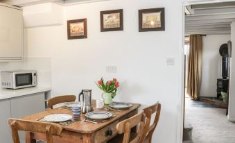 a wooden dining table with plates , cups , and a vase of flowers is set in a room with white walls and framed pictures at The Cow Shed