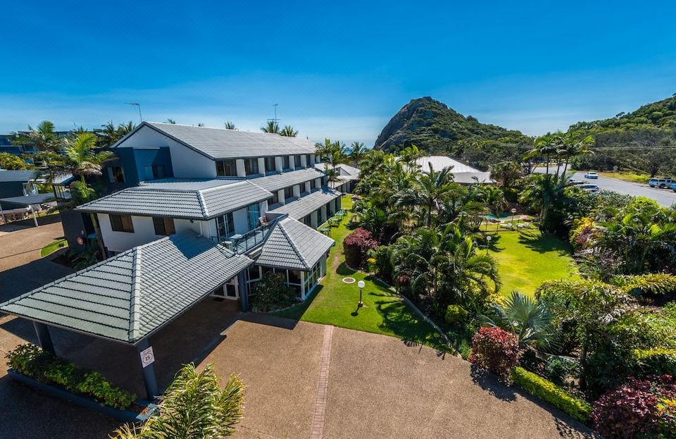 a large , two - story house with a gray roof and white walls is surrounded by lush greenery at Rosslyn Bay Resort