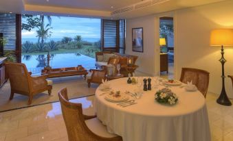 a dining room with a round table surrounded by chairs , and a view of the ocean through large windows at The Residence Zanzibar