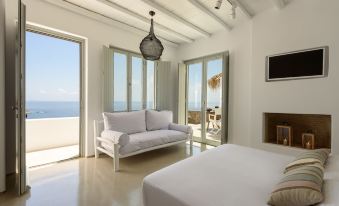 a modern living room with white walls , wooden floors , and large windows offering a view of the sea at The Summit of Mykonos