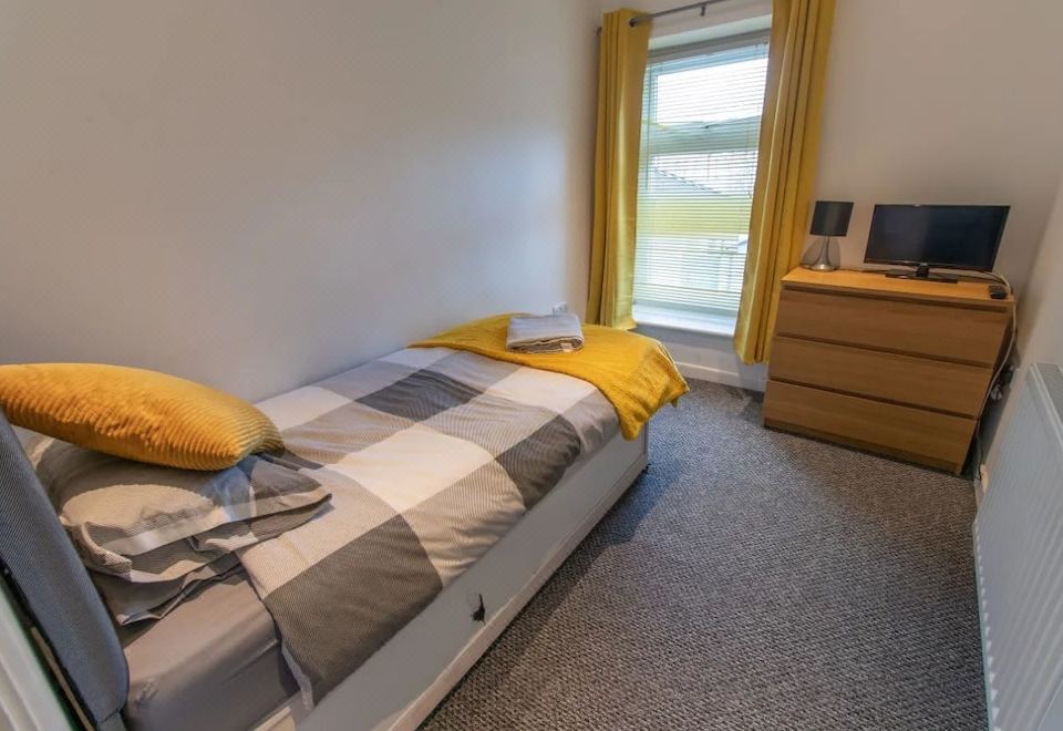 a bedroom with a bed , yellow and gray pillows , and a window with yellow curtains at Scenic Roots