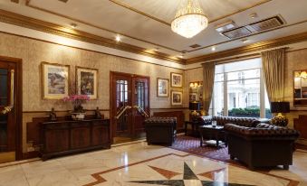 a luxurious hotel lobby with marble floors , wooden walls , and gold trim , featuring multiple couches , chairs , and a chandelier at Berjaya Eden Park London Hotel