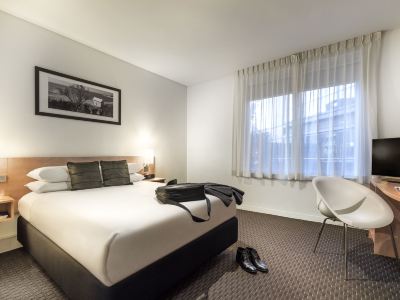 a large bed with a white comforter and black headboard is in a room with a window at Ibis Melbourne Hotel and Apartments