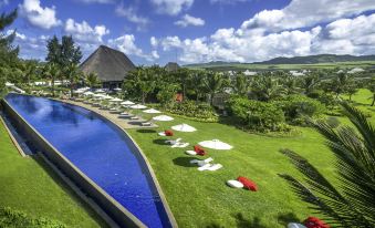a large pool surrounded by lush green grass and palm trees , with lounge chairs and umbrellas placed around the pool area at SO Sofitel Mauritius